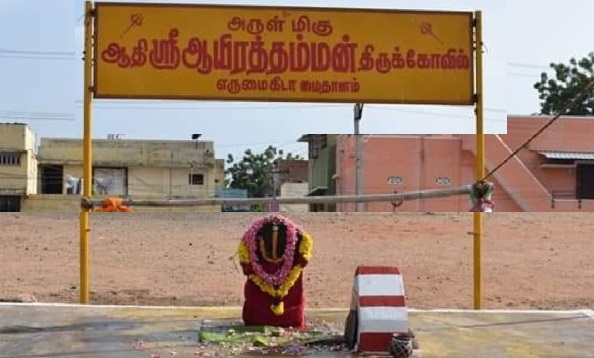 Aayirathamman temple name board in front of an idol placed in a large ground with several houses visible in the background