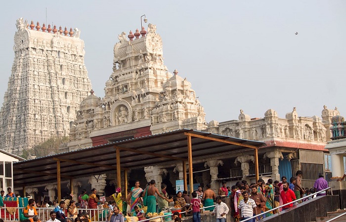 View of the majestic main gopuram and devotees gathered outside the smaller gopuram entrance of the Tiruchendur temple.