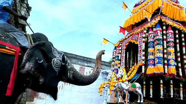 Temple elephant in front of a decorated temple car.