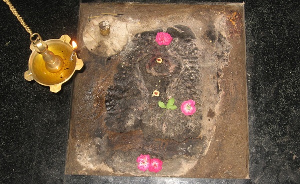 Thiruvenkadar Sivan temple sculpture, decked with pink flowers with a lamp lit on the side