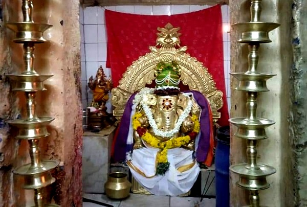 Golden idol of lord ganesh with lamps on both sides.