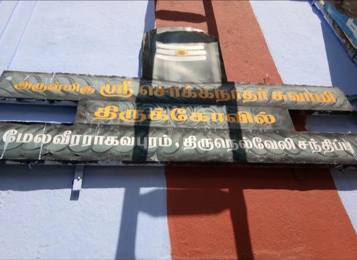Decorative nameboard hung on the blue and red temple wall at Melaveeraragavapuram Chokkalingaswamy Temple in Tirunelveli