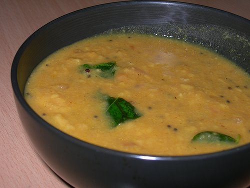 Yellow-shaded karunaikizhangu masiyal with mustard and curry leaf tempering served in a black ceramic bowl.