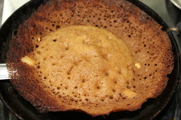 A picture of the delicious karuppatti appam with its soft, fluffy cenre and intricate, lace-like, crispy golden brown edge.