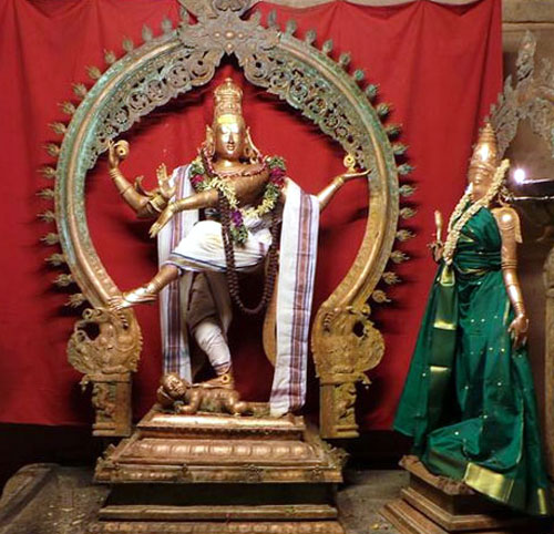 Bronze statue of Lord Natarajar in his classic dance pose. He is enrobed in a white attire, wearing a white angavastram and flower garlands. Goddess Parvathi's statue faces the Lord from his left side. She is enrobed in a green silk attire and decorated with a garland.