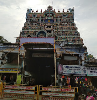 Front view of the Nellaiappar temple gopuram, main entrance, and the shops next to the entrance, and the police barricades on the road.