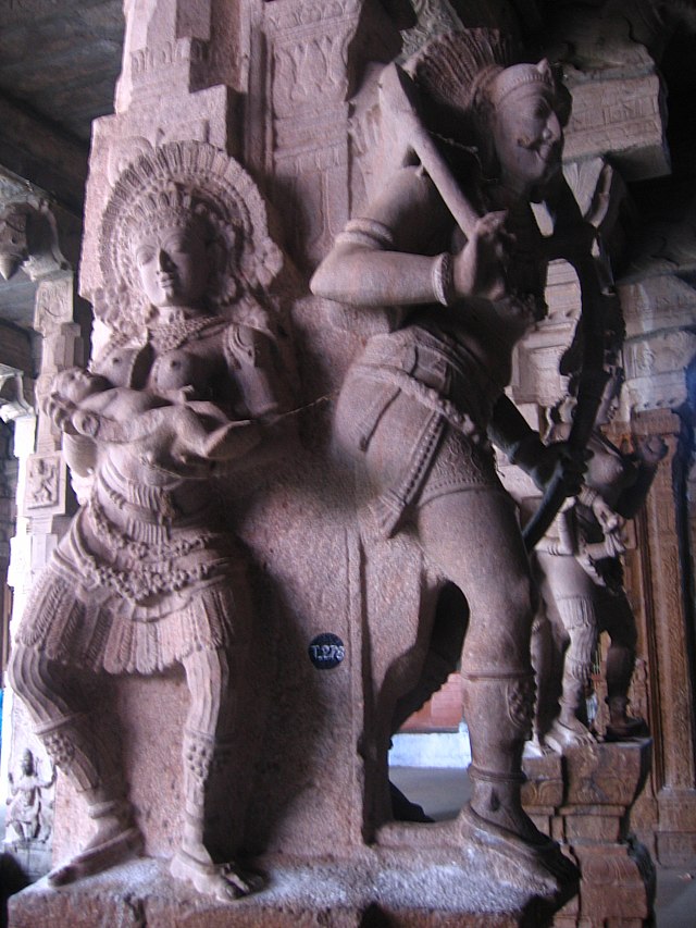 A huge stone pillar engraved with a figure of a goddess holding a child on one side and a man with a bow and arrow on the other side.