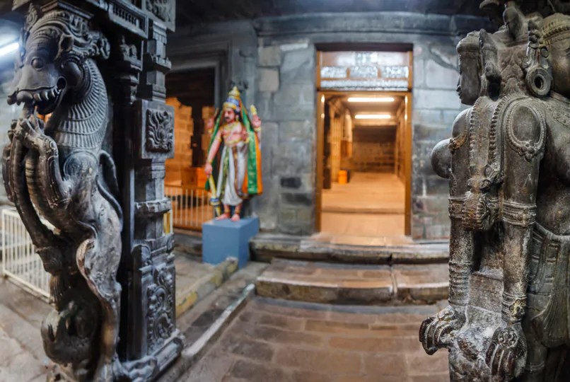 Two stone statues with a perfectly lighted temple hallway in the background.