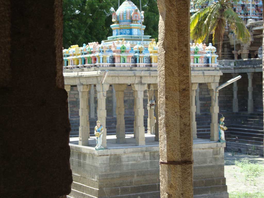 A colourful mandapam at the background with a stone pillar in the front.